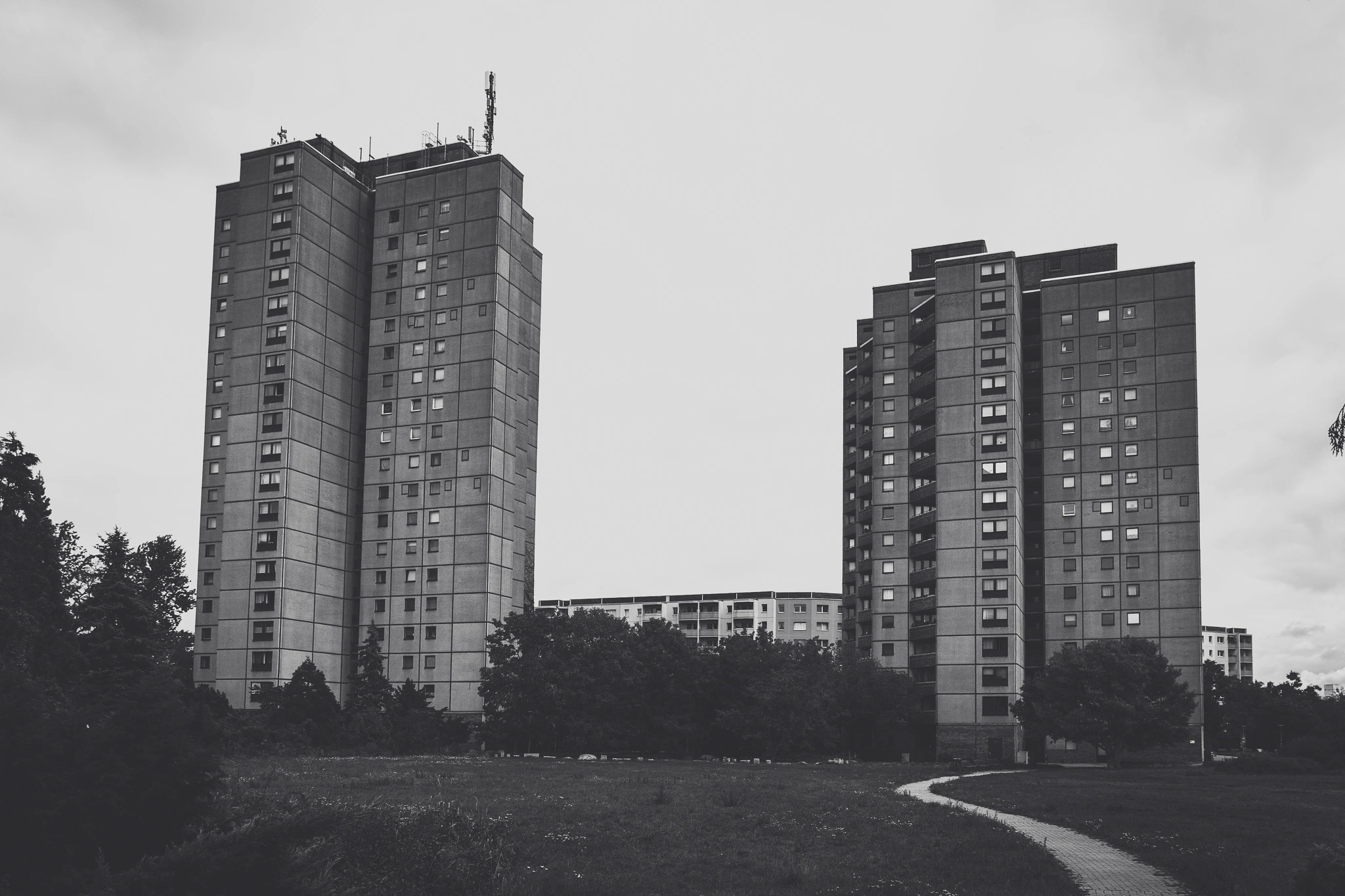 Two Plattenbau tower blocks behind a park path, black and white