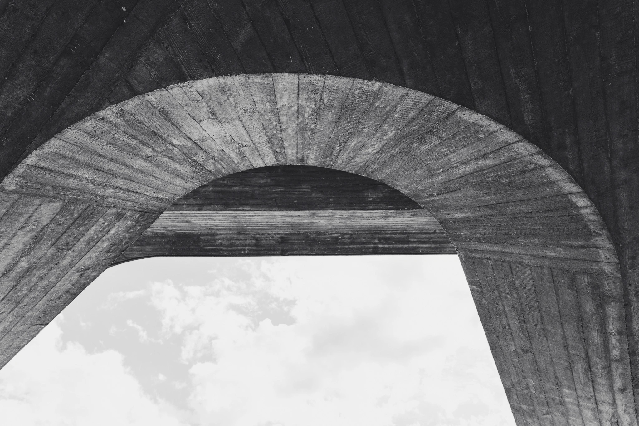Board-marked concrete arch seen from below, black and white