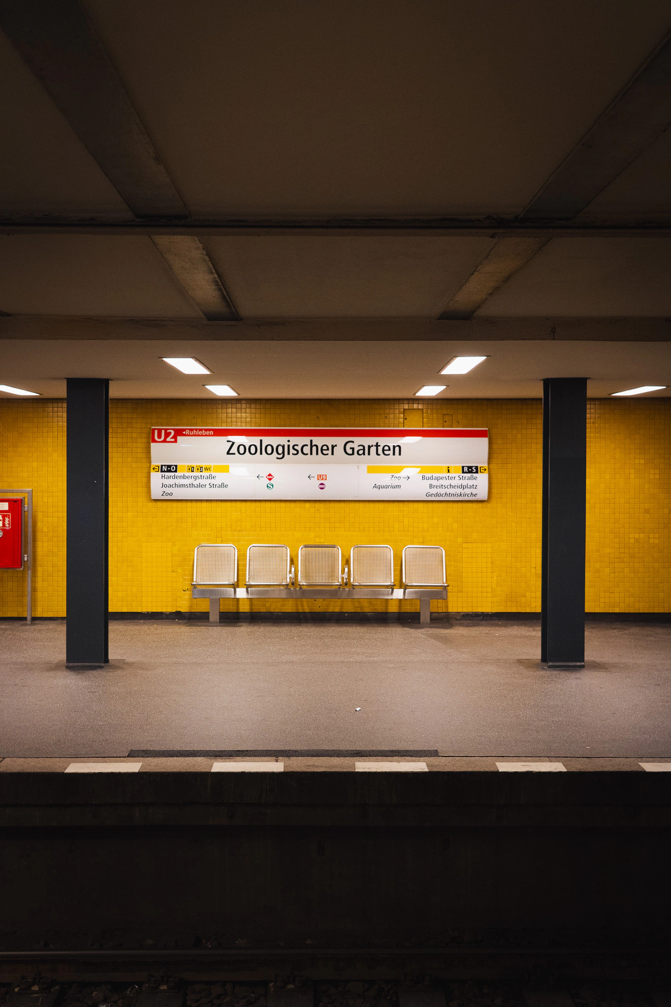 Yellow-tiled platform of U-Bahnhof Zoologischer Garten with empty metal benches
