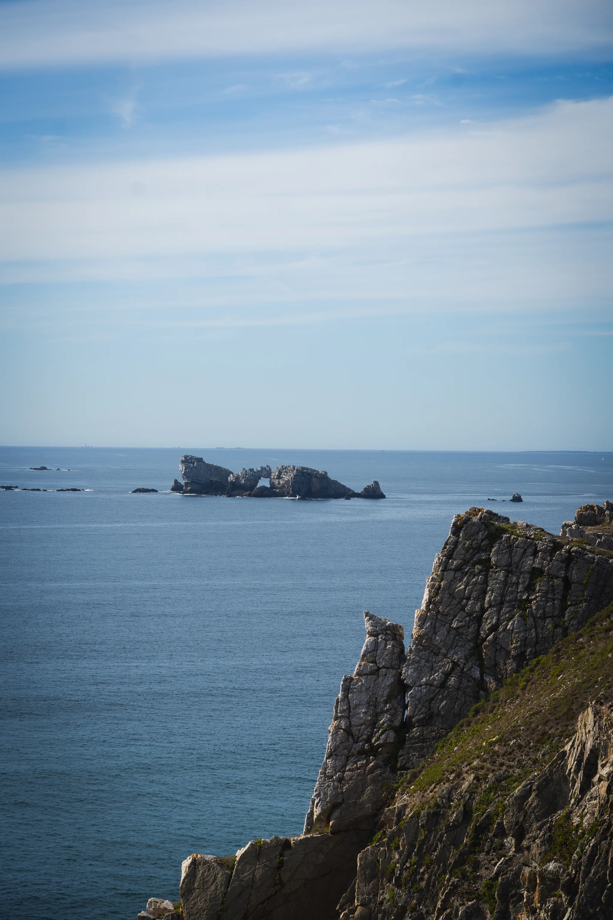 Rock island with a natural arch offshore, dark cliff in the foreground
