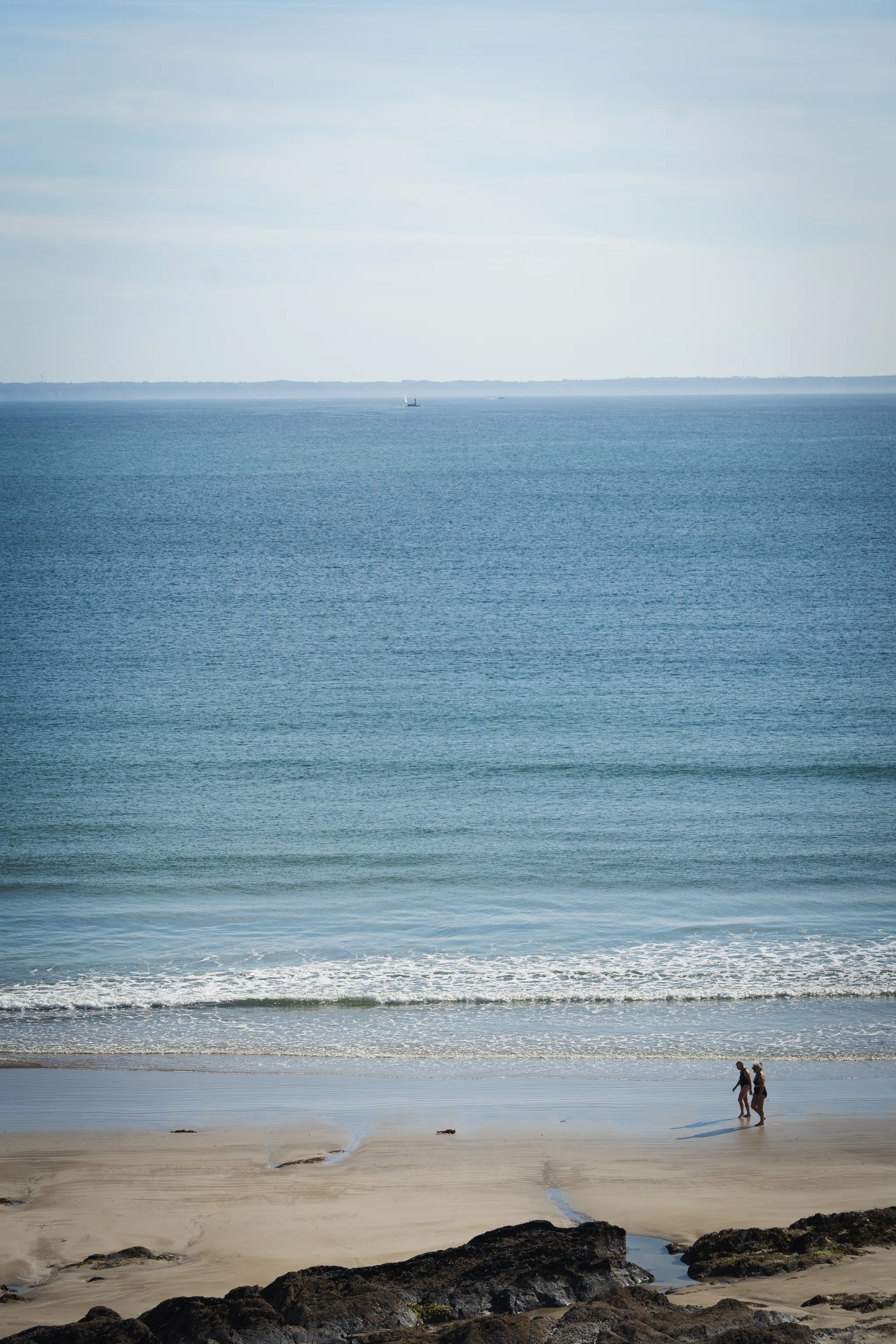Two small figures on a wide sandy beach at the waterline