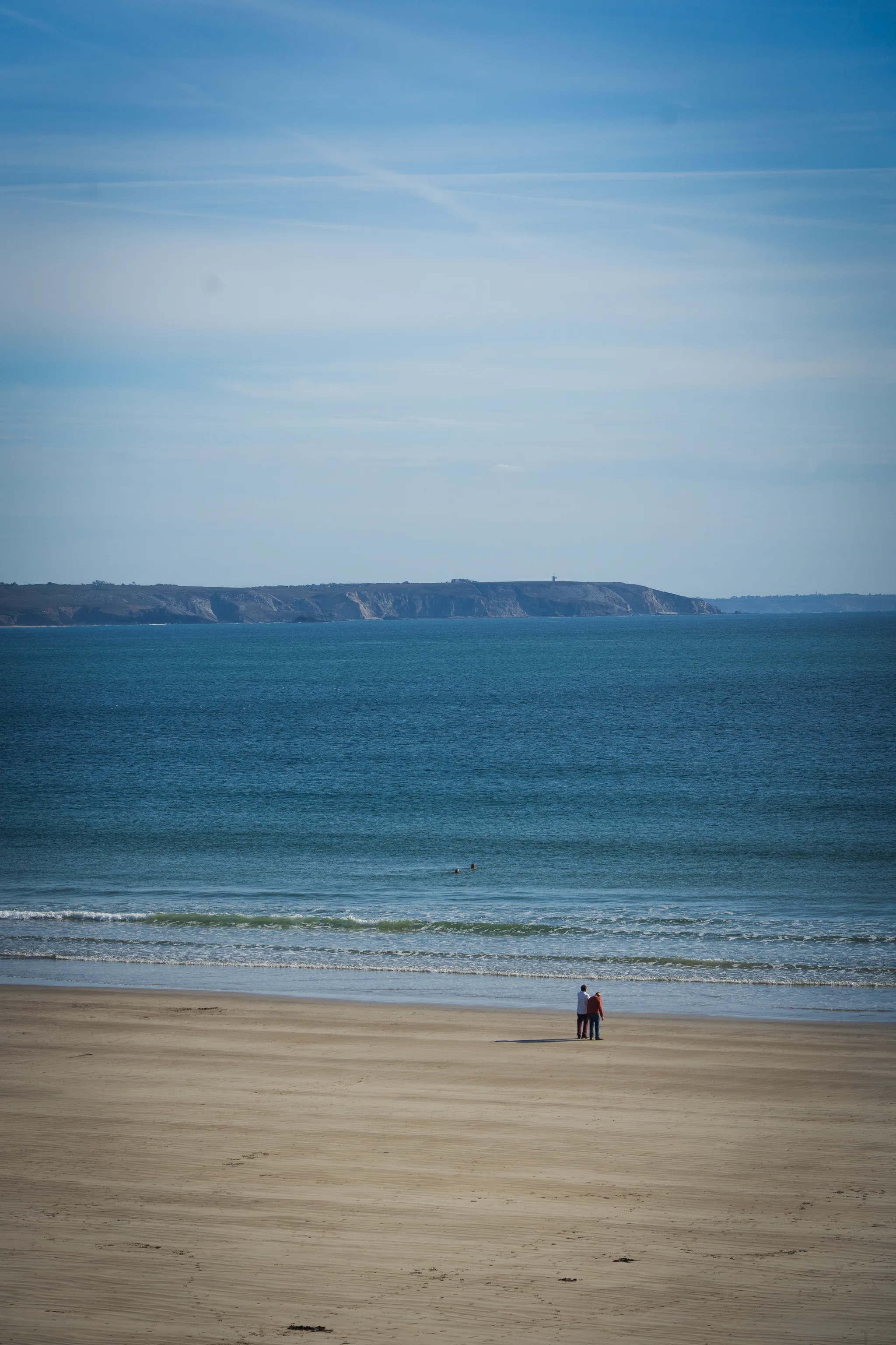 A pair of walkers on an empty beach, a headland across the bay
