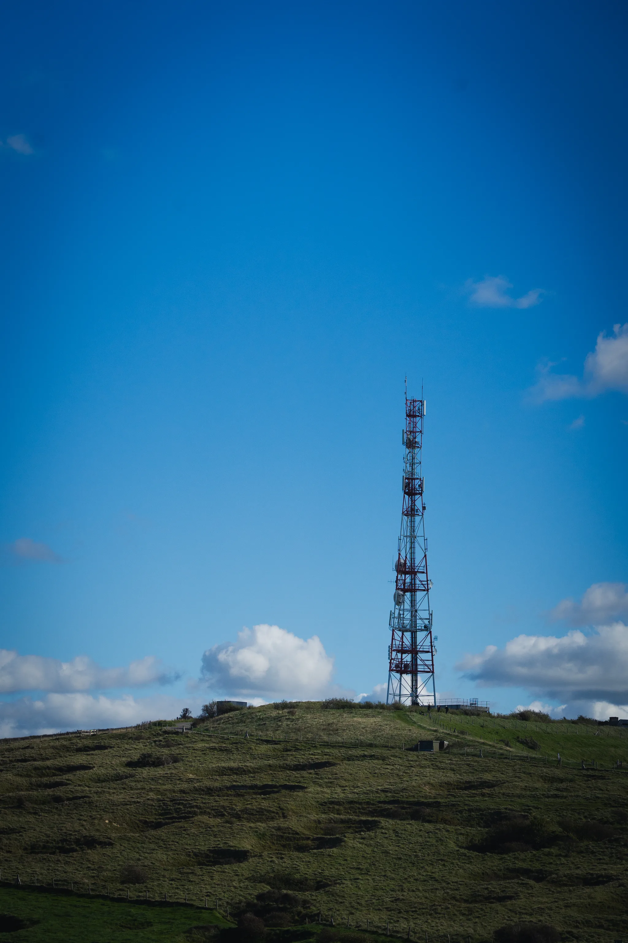 Lattice radio mast on a green hill against blue sky