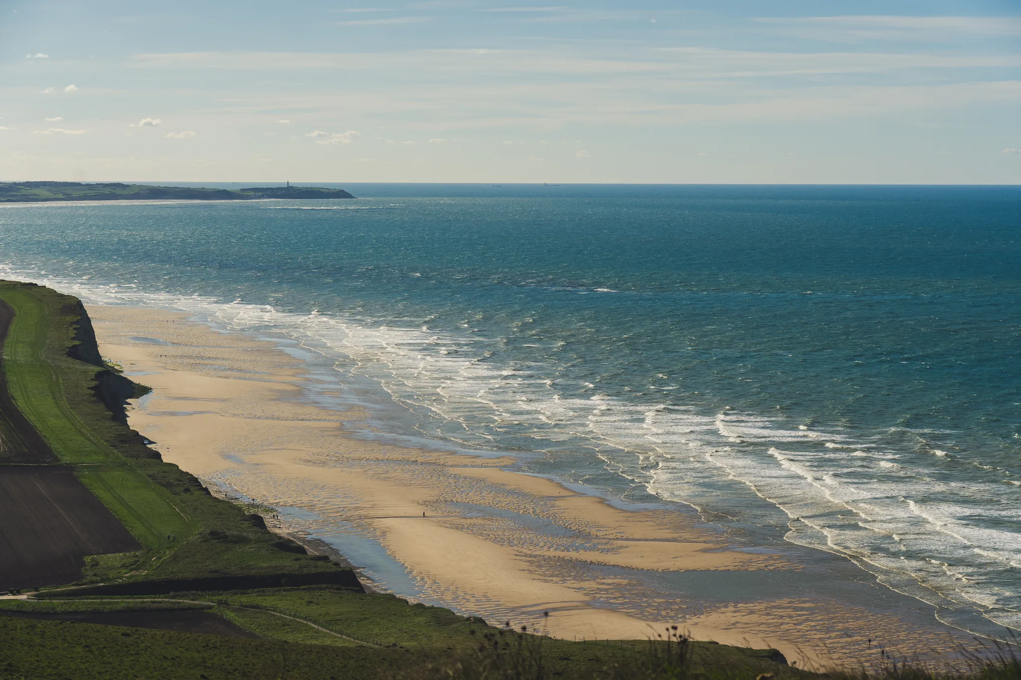 Wide sandy beach and surf seen from the cliff top, a headland in the distance