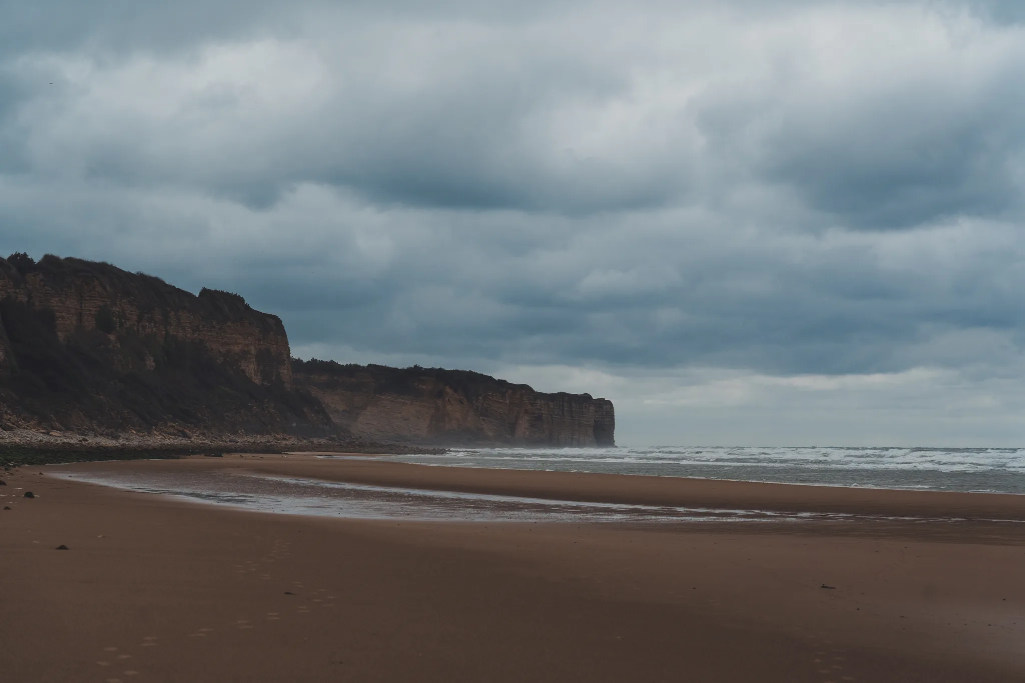Cliffs and a curving beach at low tide under storm clouds