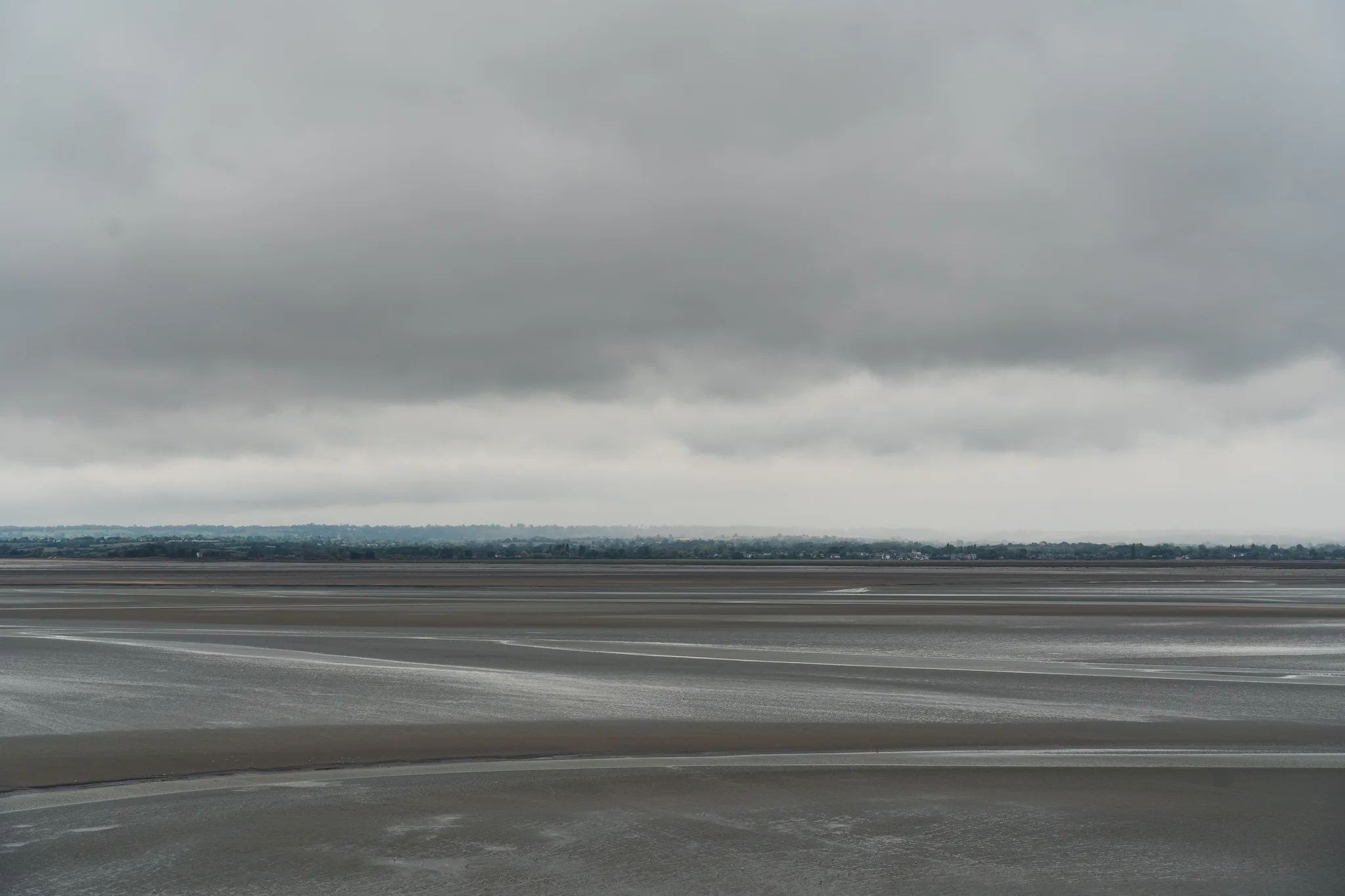 Flat sand and water stretching to the far shore under low cloud