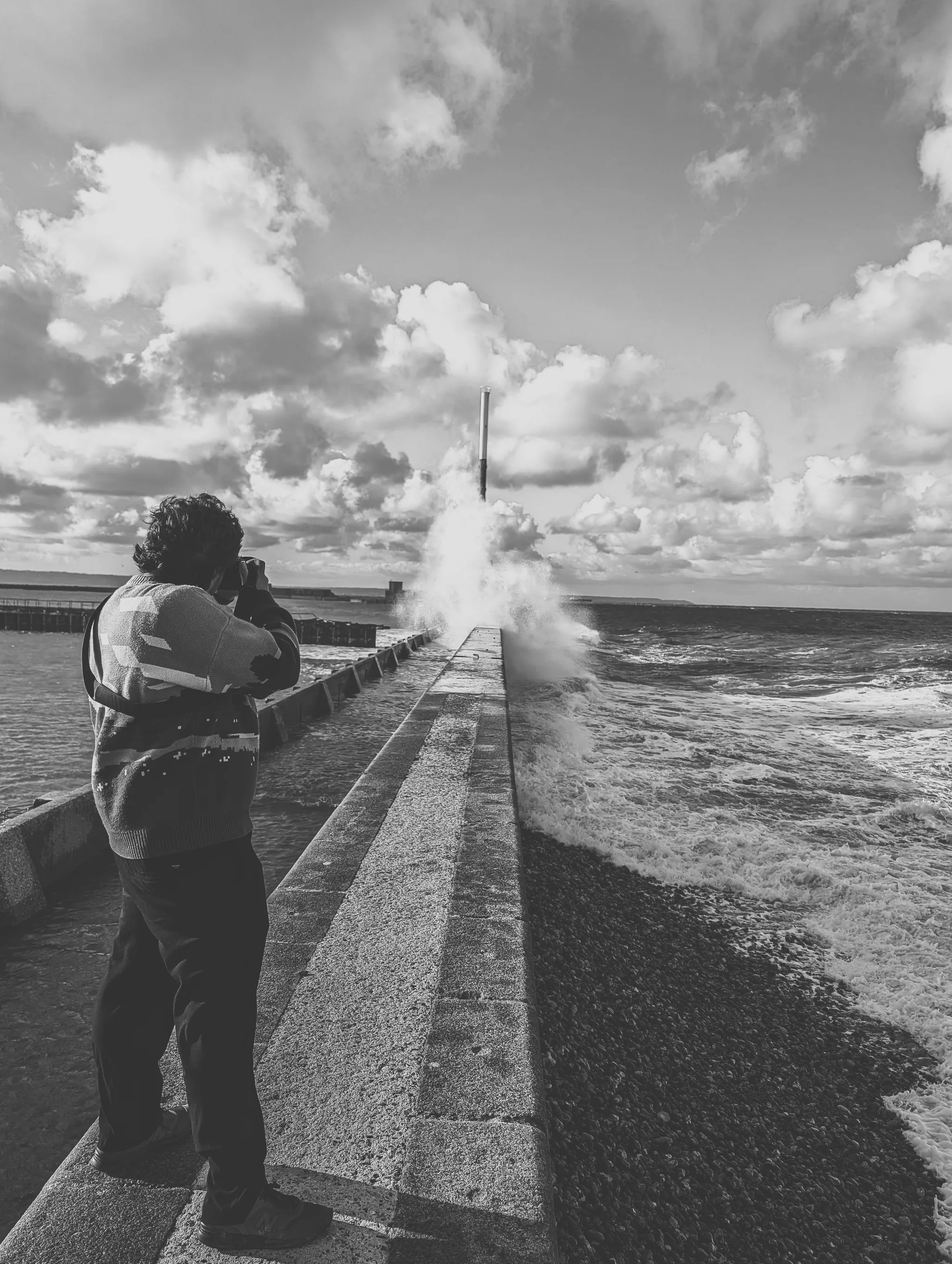 Person photographing waves breaking at the end of a jetty, black and white