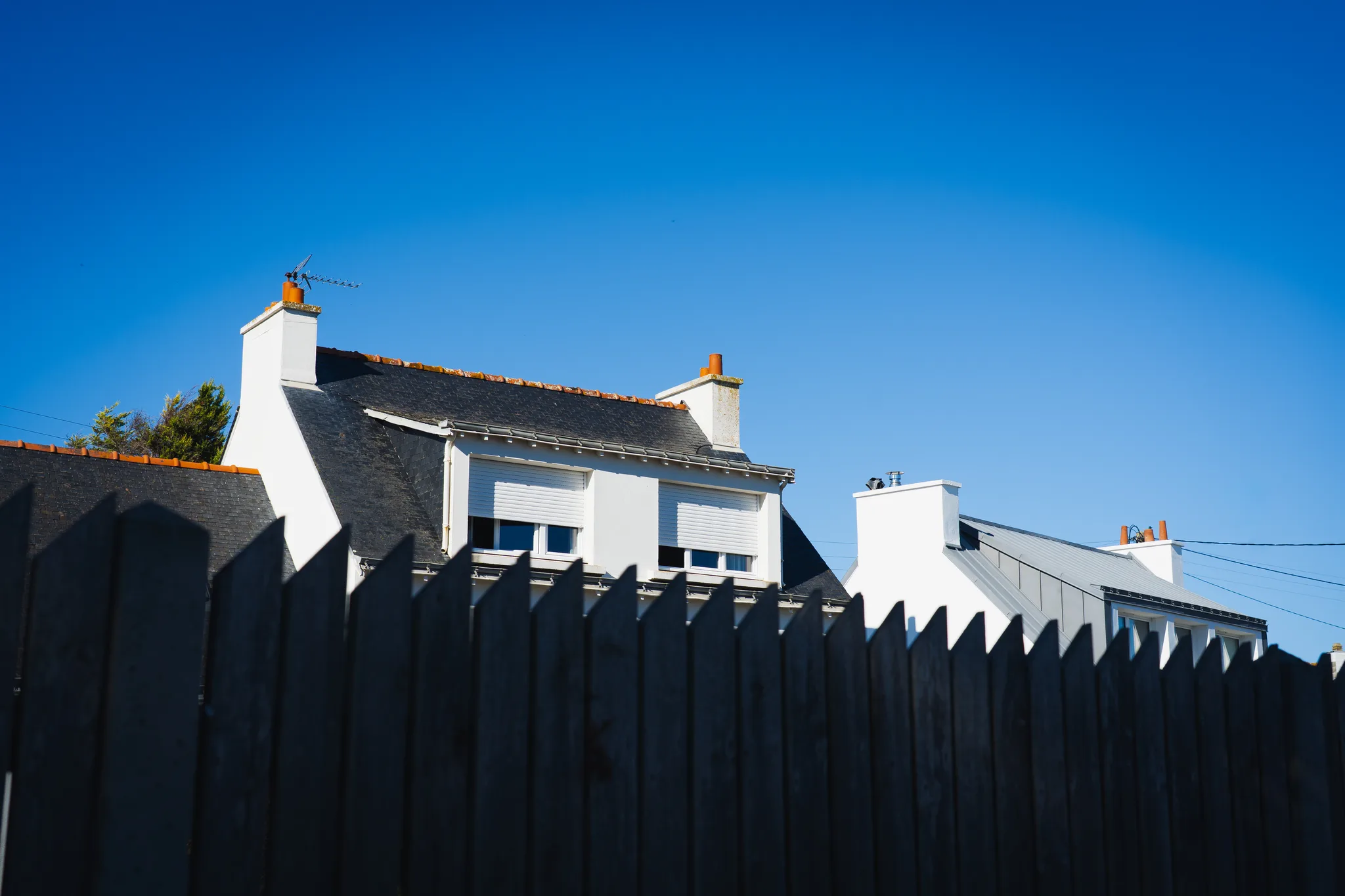 White houses with slate roofs behind a black wooden fence under blue sky