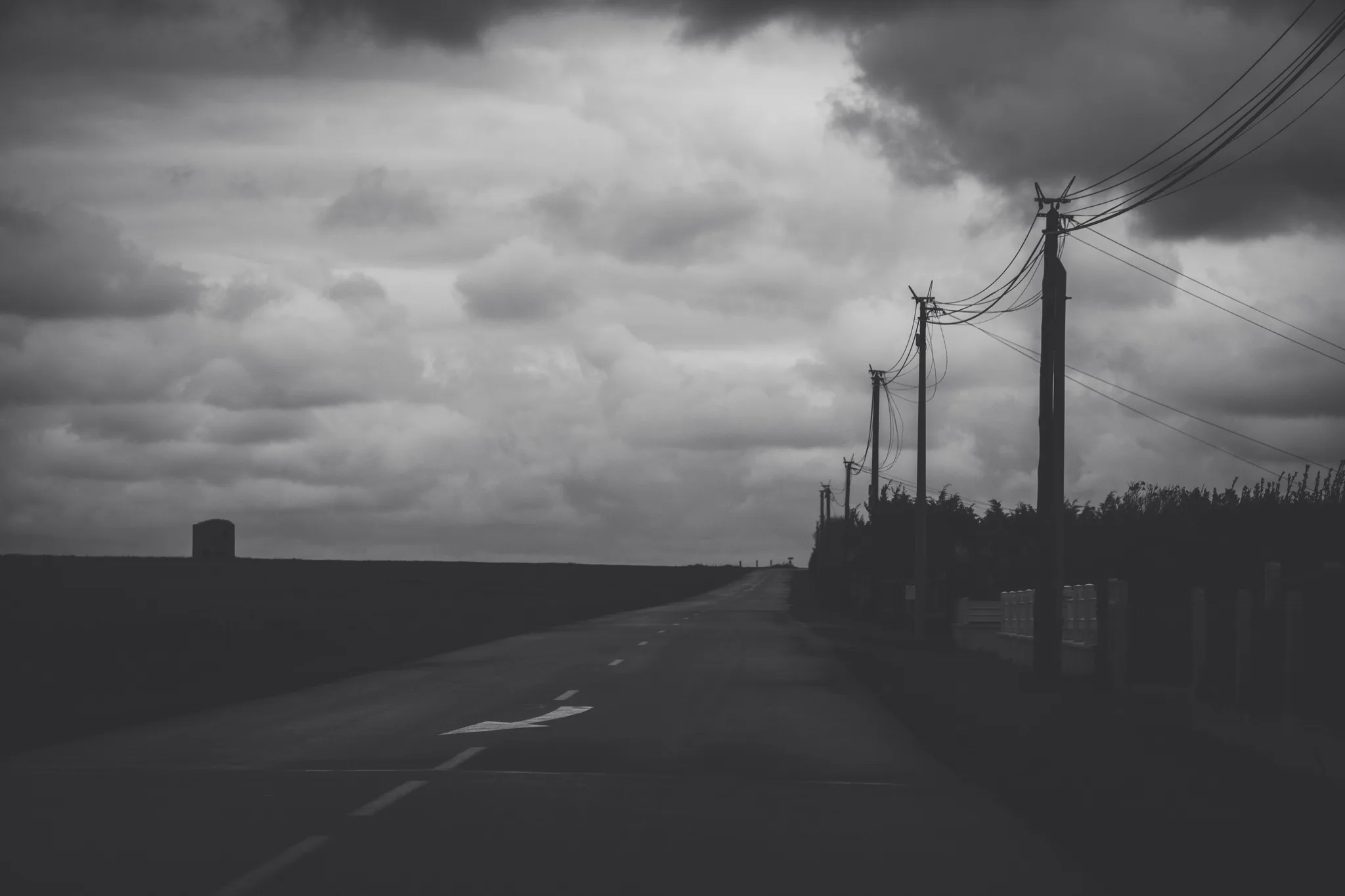 Empty road with power lines under storm clouds, black and white