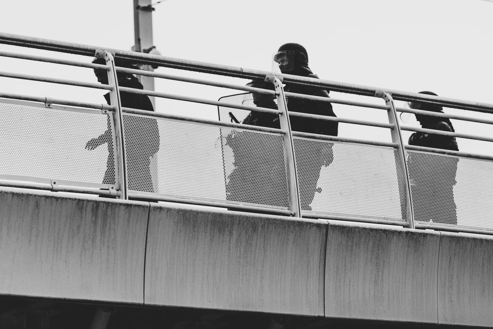Three riot police officers in silhouette behind the bridge railing, black and white