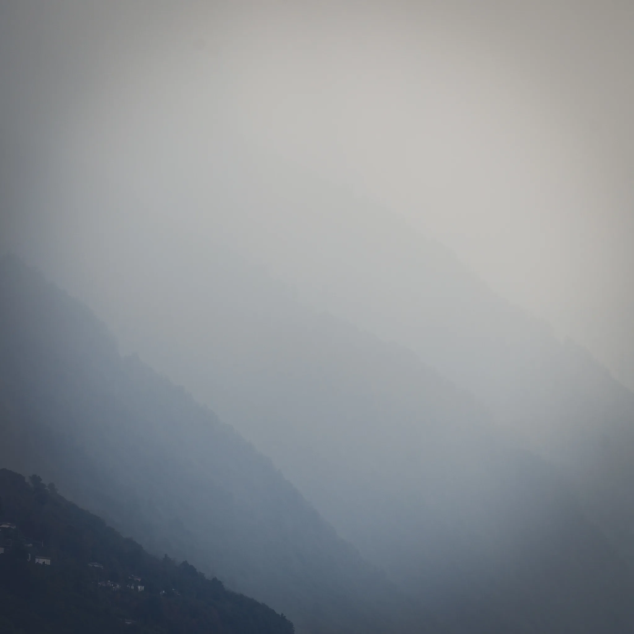 Layered mountain ridges fading into fog, a few houses on the nearest slope