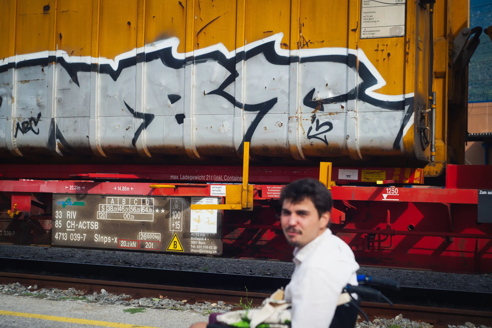 Man in a white shirt in front of a graffiti-covered yellow freight container on a red Swiss rail wagon