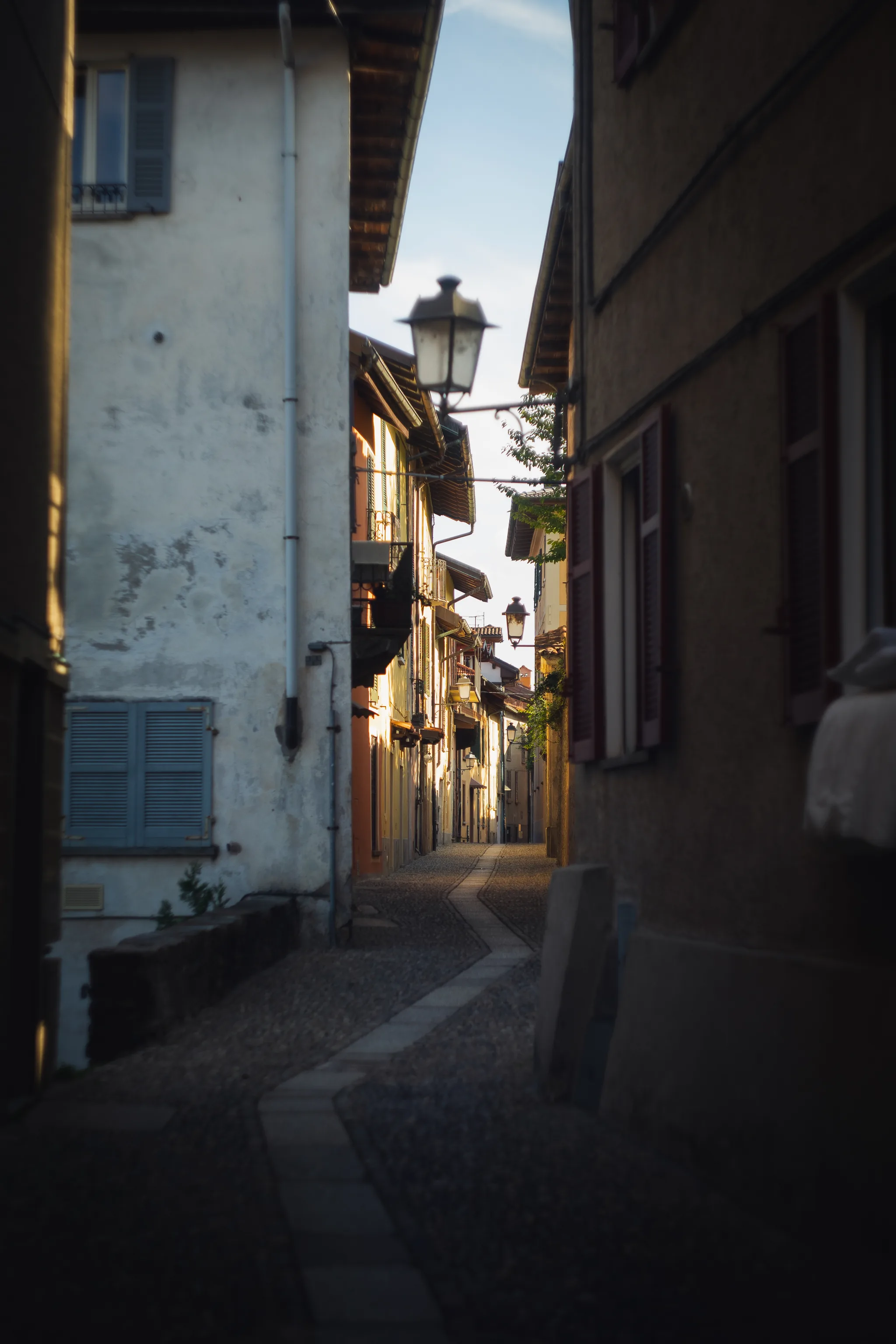 Shaded lane with blue shutters and hanging lanterns, sunlit houses further down