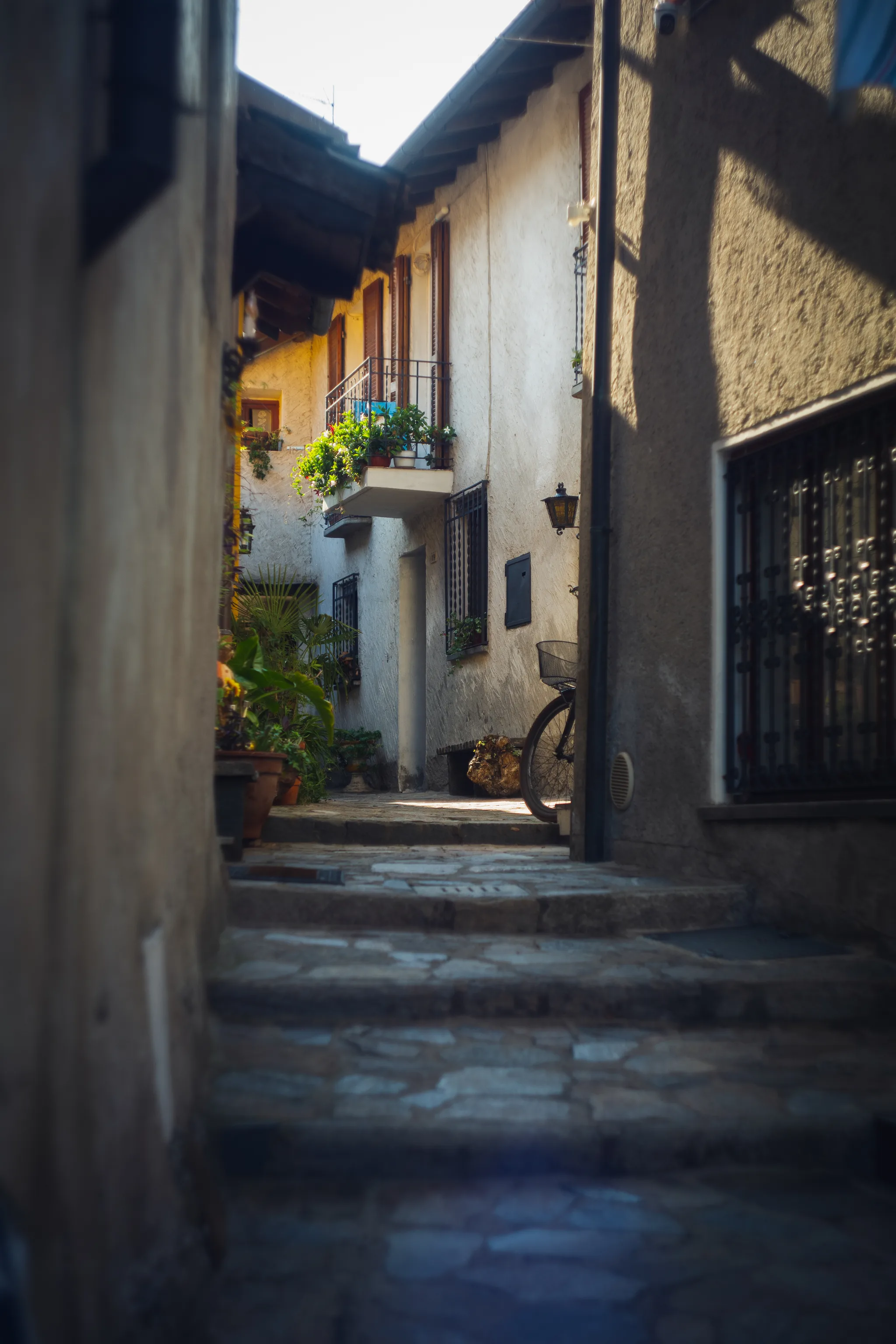 Stone steps leading to a house with a flower-filled balcony and a bicycle by the door