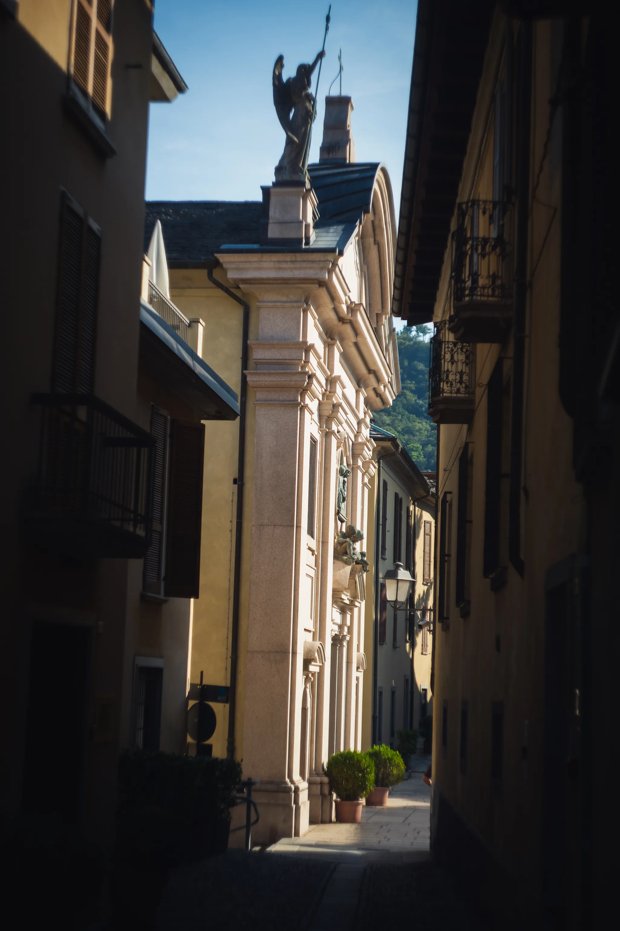 Church facade topped by an angel statue at the end of a narrow shaded street