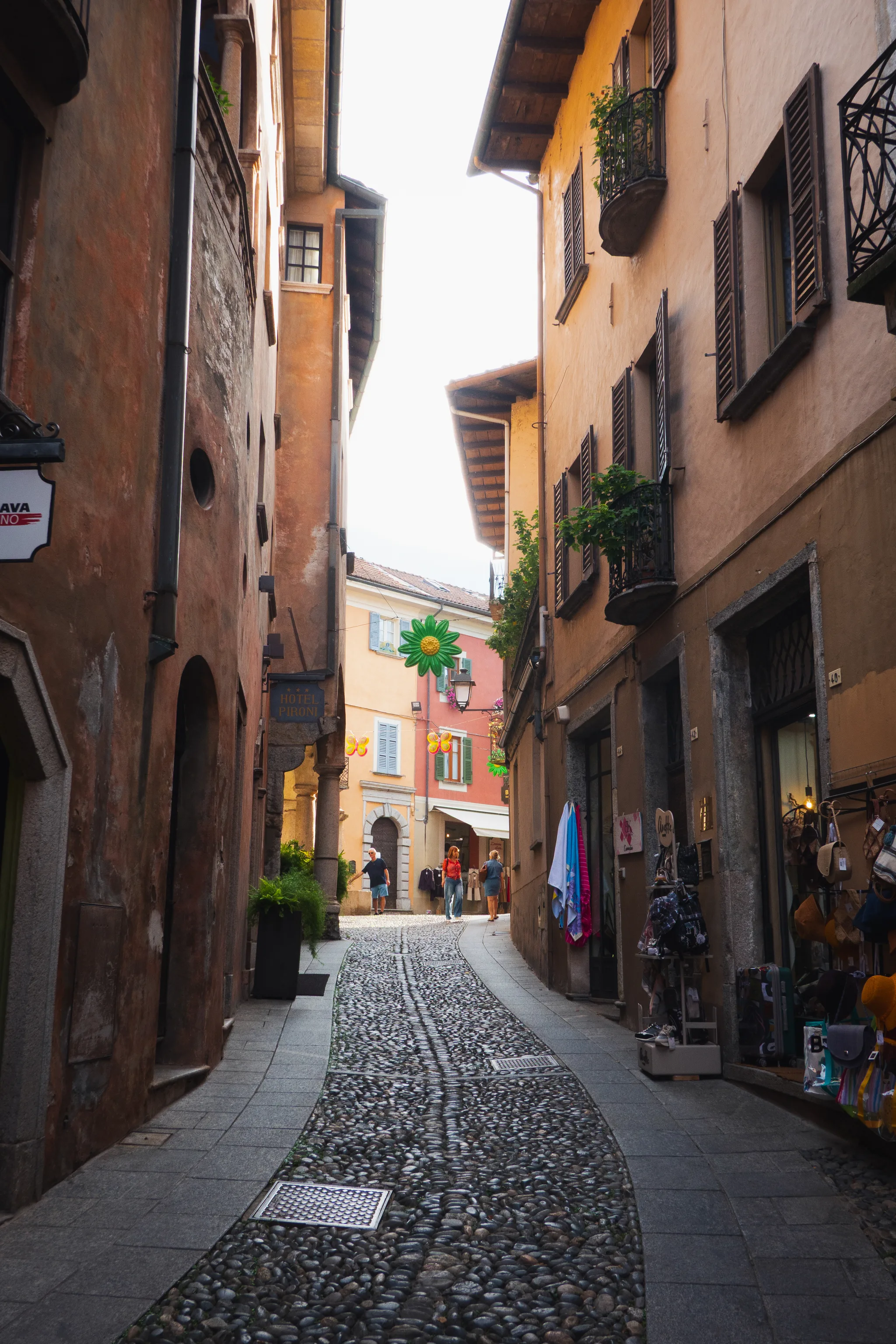 Cobbled lane between ochre houses with shops selling towels and bags, a flower decoration at the end