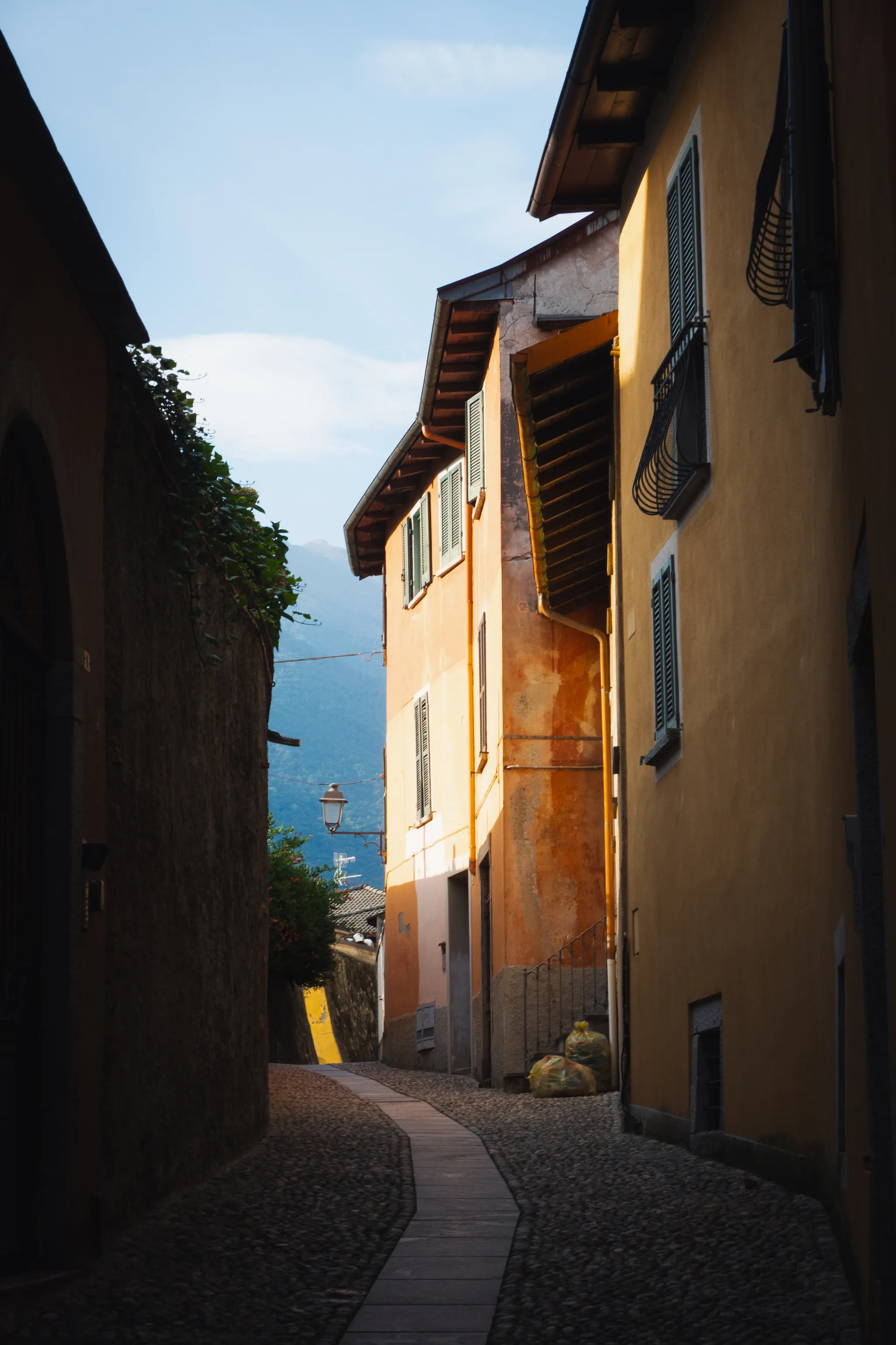 Narrow cobbled lane with a stone strip in the middle, orange house fronts lit by the sun and a mountain behind