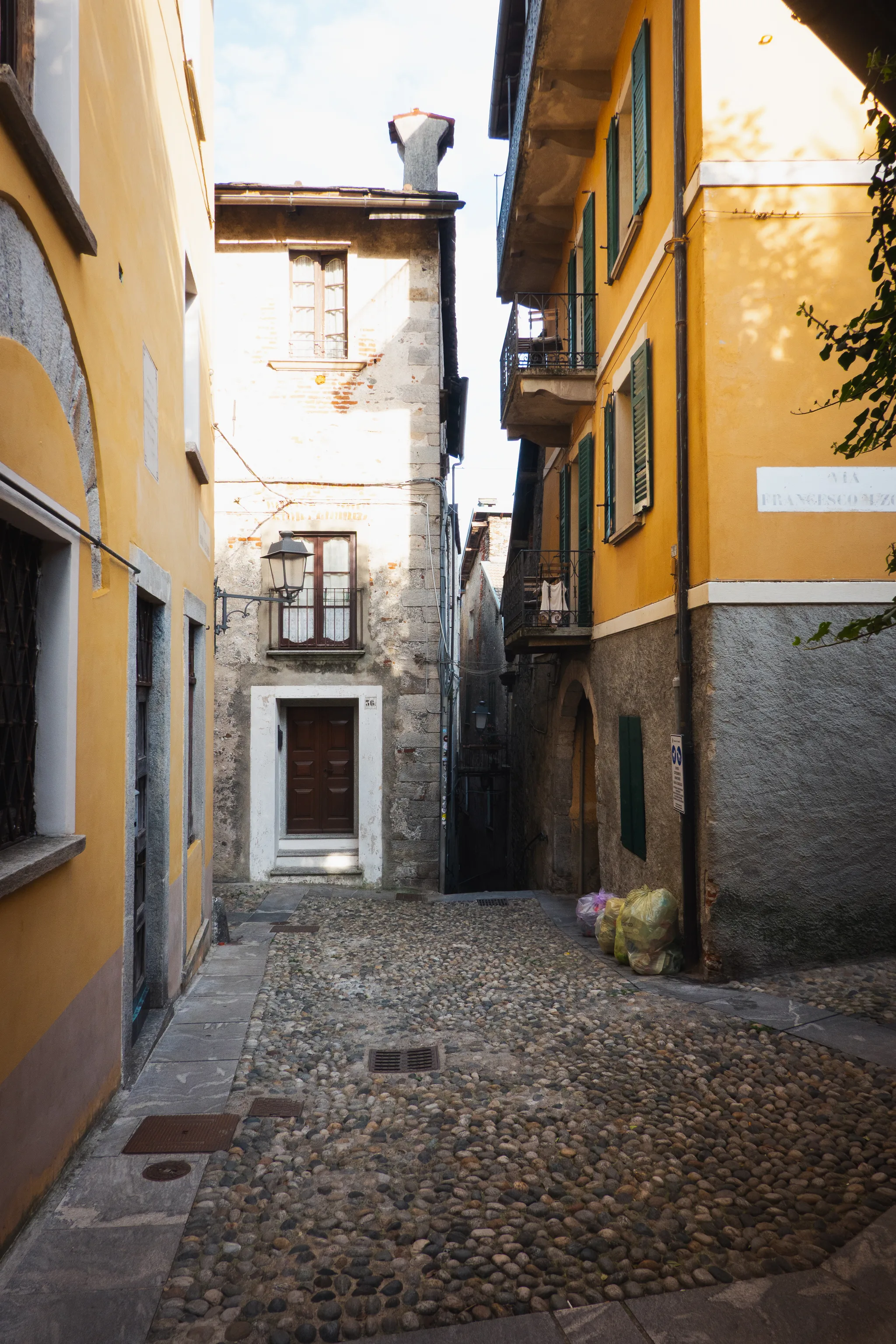 Cobbled square between a yellow house with green shutters and an old stone house with a lantern