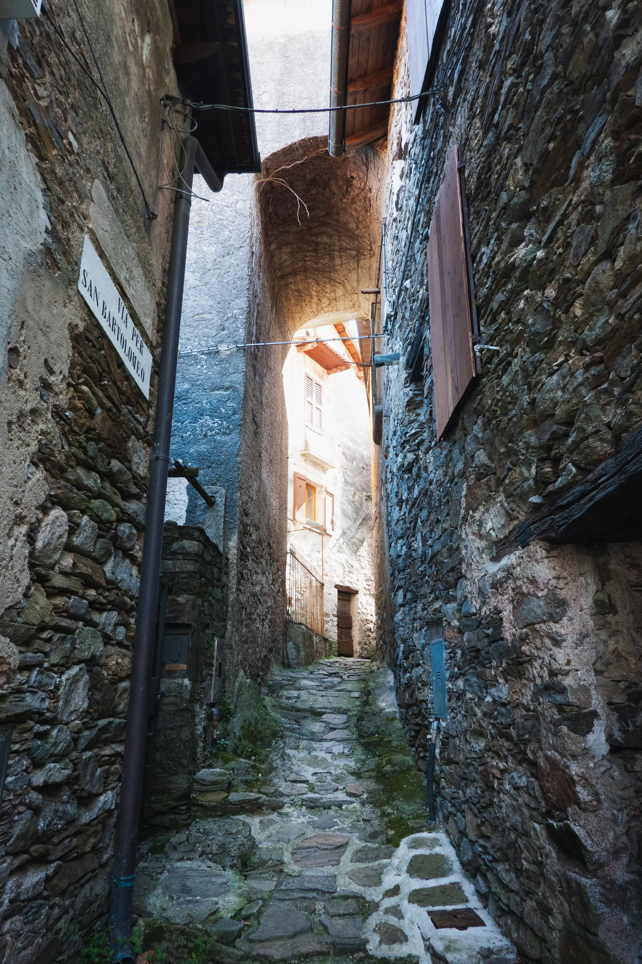 Narrow stone alley under an arch, with a Via per San Bartolomeo sign on the wall