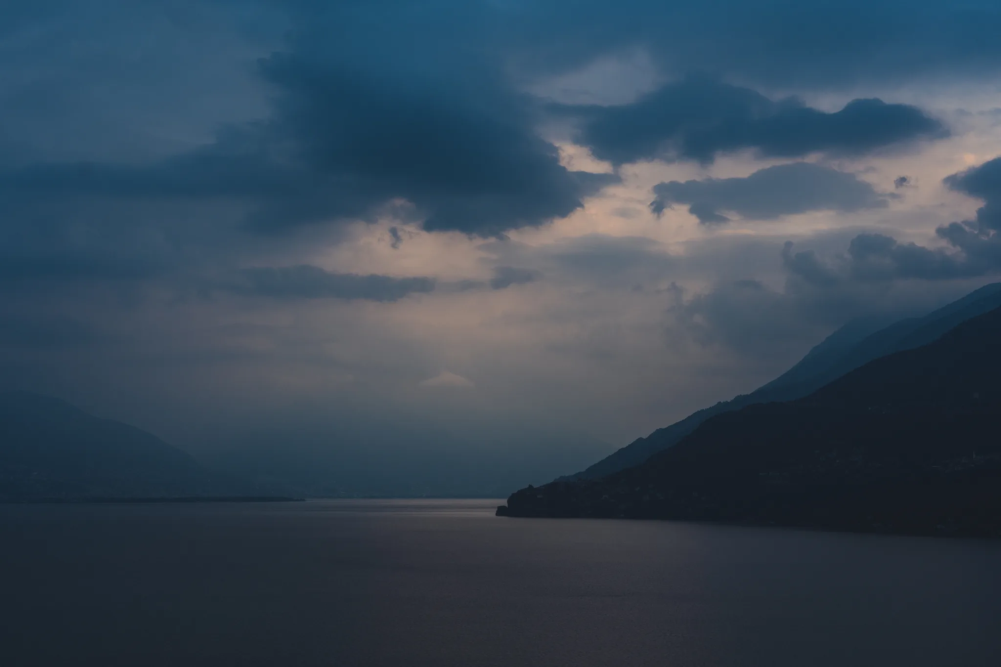 Dark clouds over the lake at blue hour, a mountain slope dropping into the water on the right